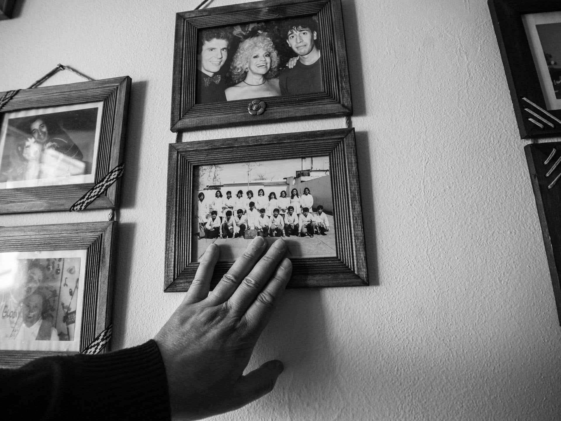 A hand reaching toward black-and-white family photographs framed on a wall
