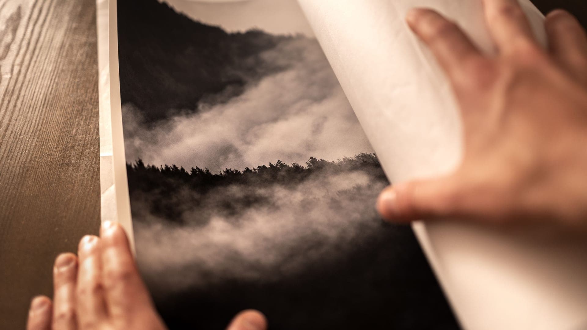 A rolled poster being flattened on a table beside an empty frame