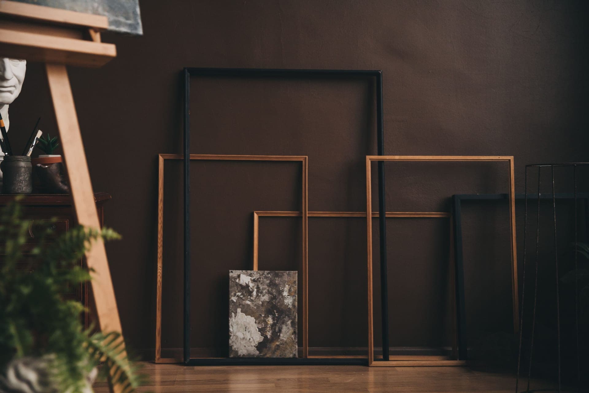 Stacked wooden and black picture frames leaning against a plaster wall
