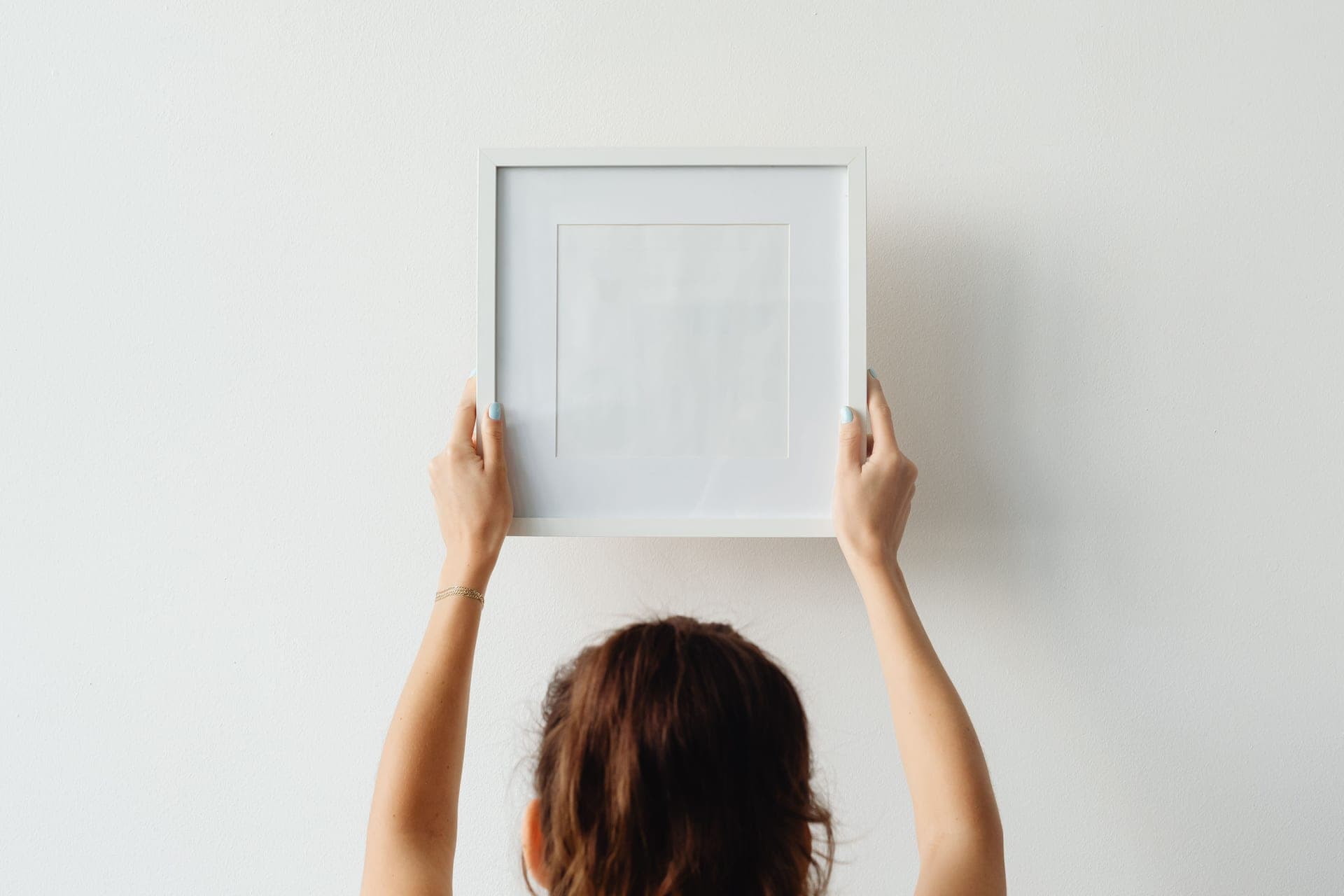 A framed print held flat against a pale apartment wall during hanging